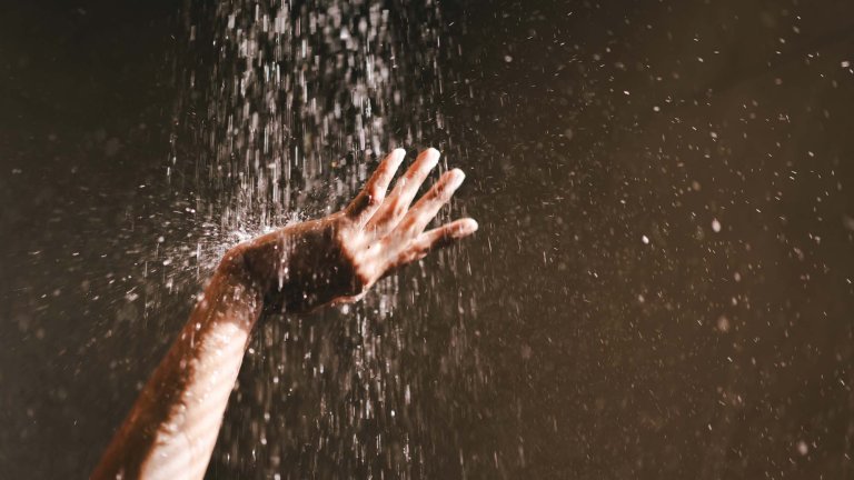 Close-up of a female's hands reaching toward the water stream of a shower under the bright sun. The image captures the sensation of cooling off, physical connection with nature, and the beauty of simple rituals. Minimal, sunlit aesthetic, themes of refreshment, tactility, mindfulness, and body awareness.
