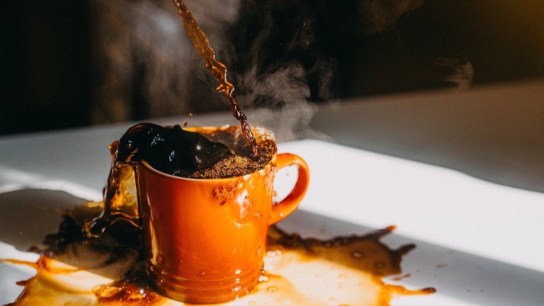 Stream of coffee pouring into an overflowing coffee mug on a white table
