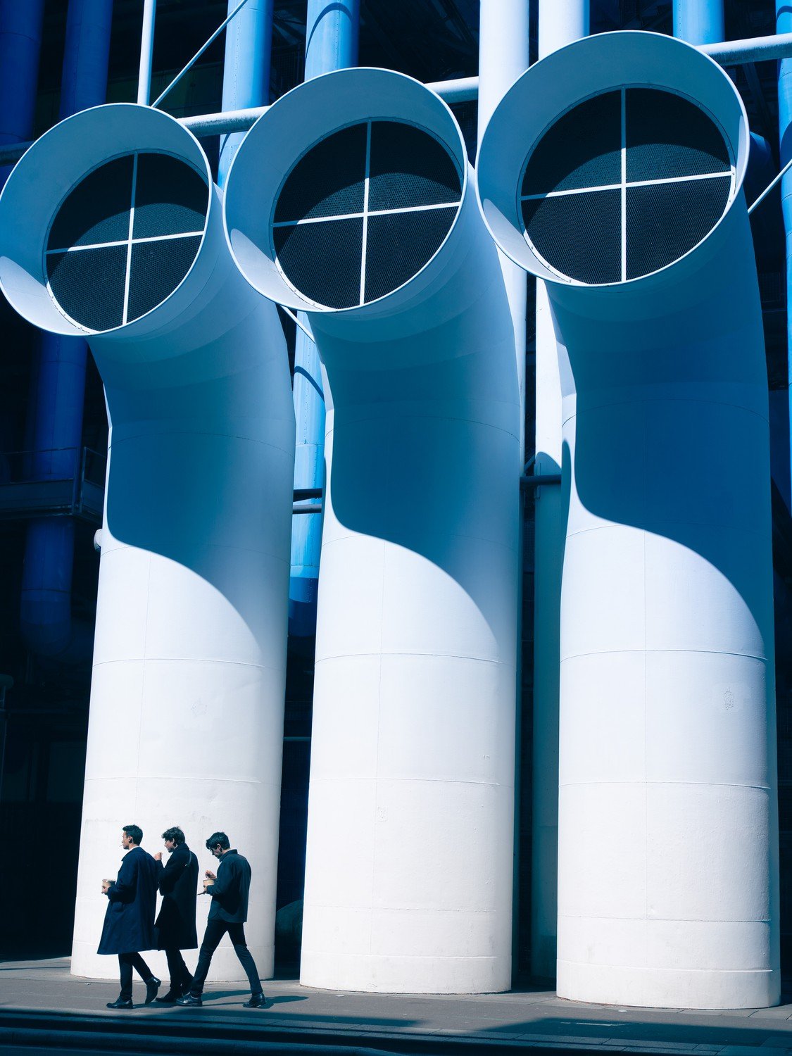 three men walking in front of large tubes