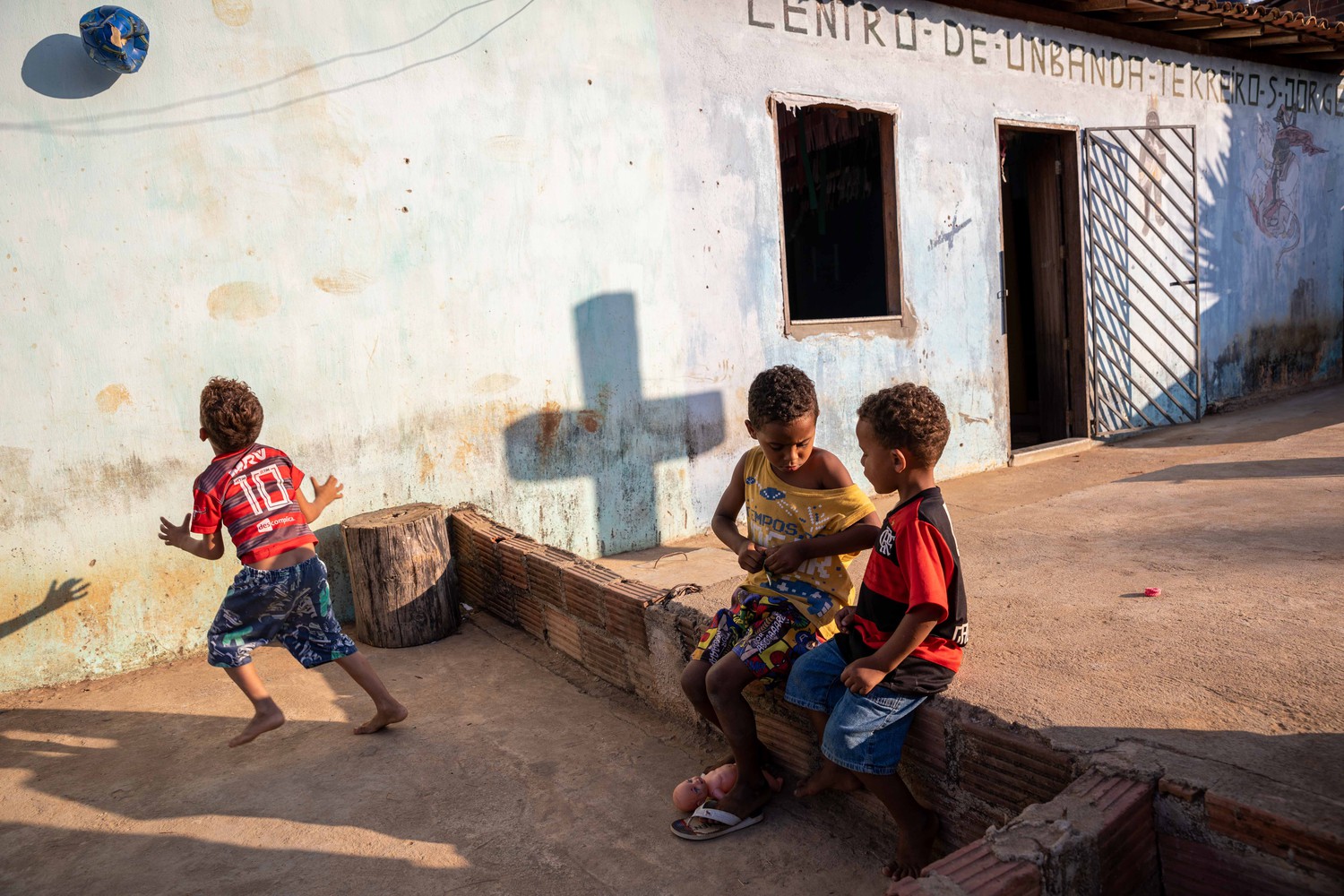 three children outside a building. the shadow of a cross on the wall