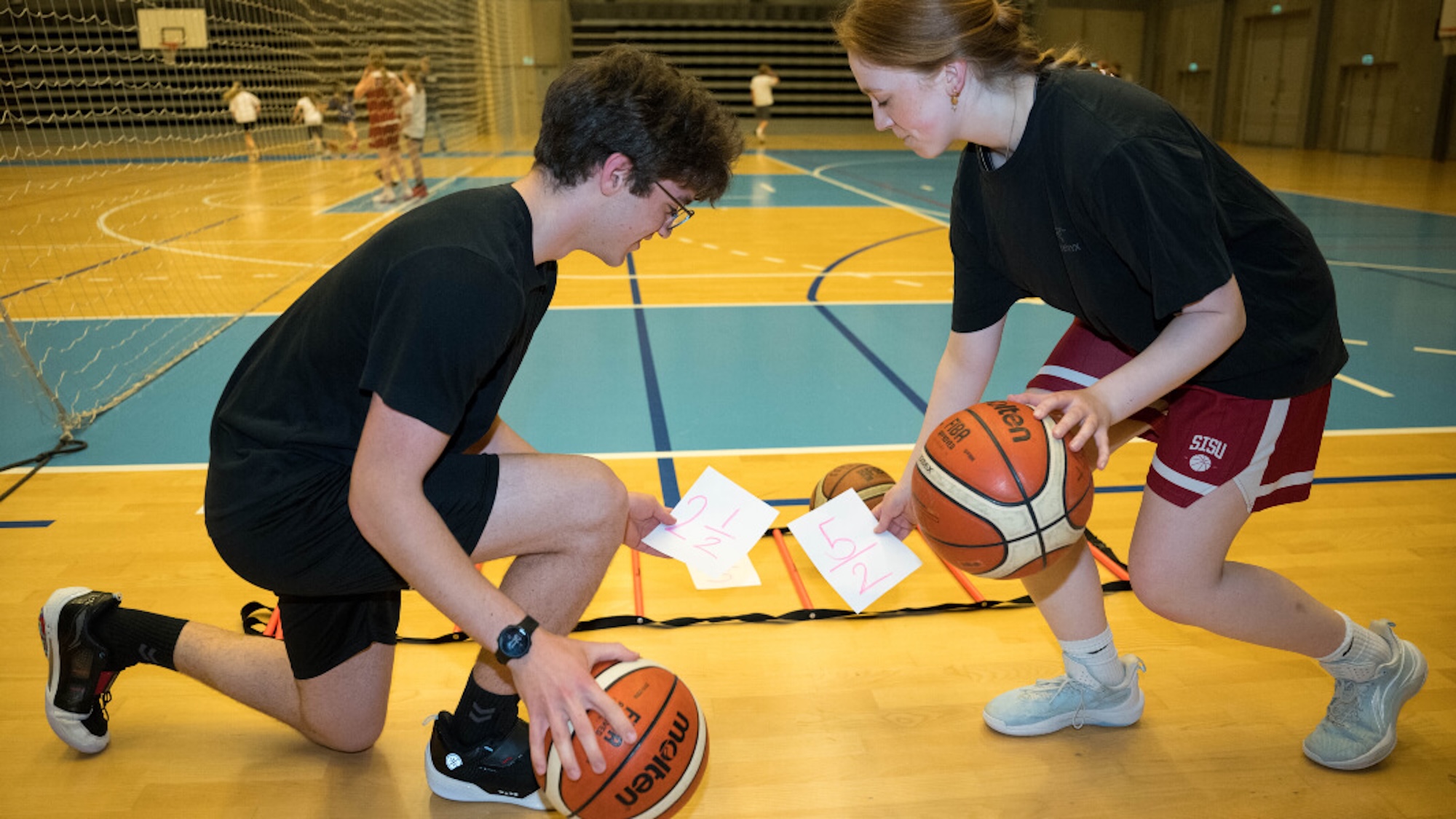 A student and teacher dribbling basketballs while holding fractions math cards