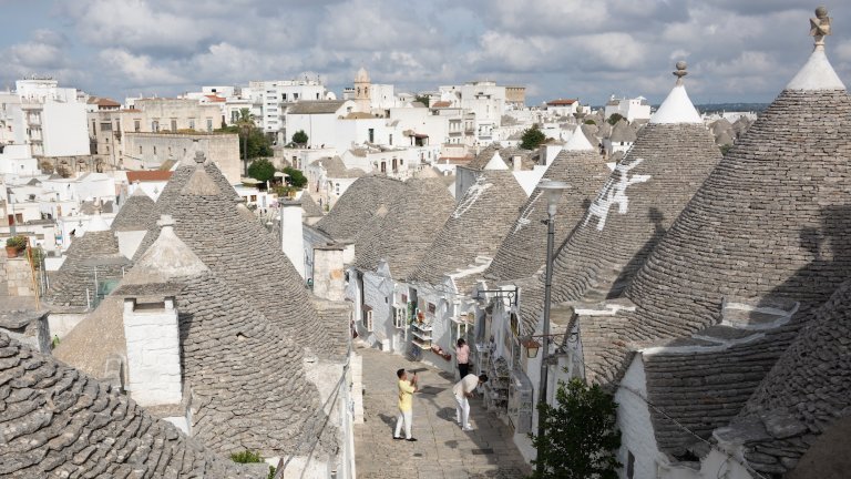 13 October 2025, Italy, Alberobello: Tourists stand among the trulli of Alberobello, the whitewashed limestone houses with the typical conical roofs. Photo: Sebastian Kahnert/dpa (Photo by Sebastian Kahnert/picture alliance via Getty Images)