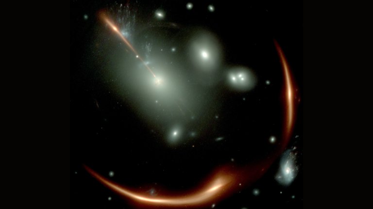 James Webb Space Telescope (JWST) image of the highly distorted red galaxy MRG-M0138 seen through a foreground cluster of galaxies (white sources). Via the phenomenon of gravitational lensing, the same background galaxy is multiply imaged four times and the white square shows the most magnified image which was studied by Newman and colleagues using the NIRSpec Integral Field Spectrograph onboard JWST. The data measures the velocity for each portion of the image within the white square. The top bar shows an angular scale of 5 arcsec. Credit: NASA/JWST