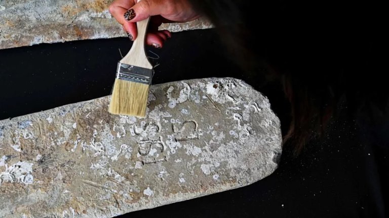 Woman's hand holding brush to clean 17th century lead ingot