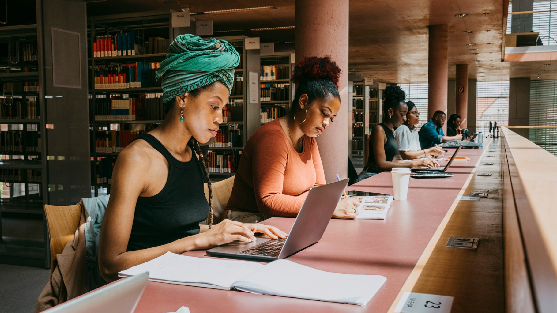 Woman wearing turban using laptop while sitting with friend in library