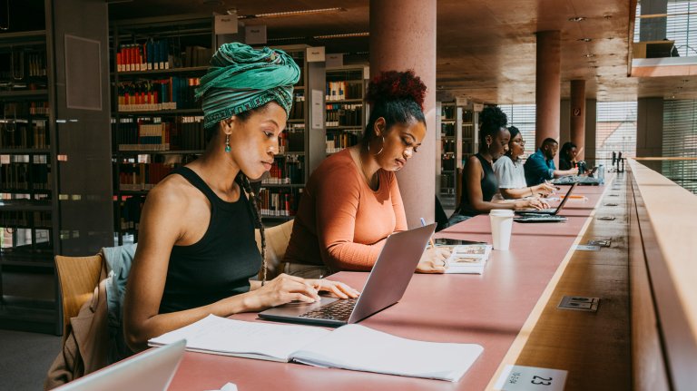 Woman wearing turban using laptop while sitting with friend in library