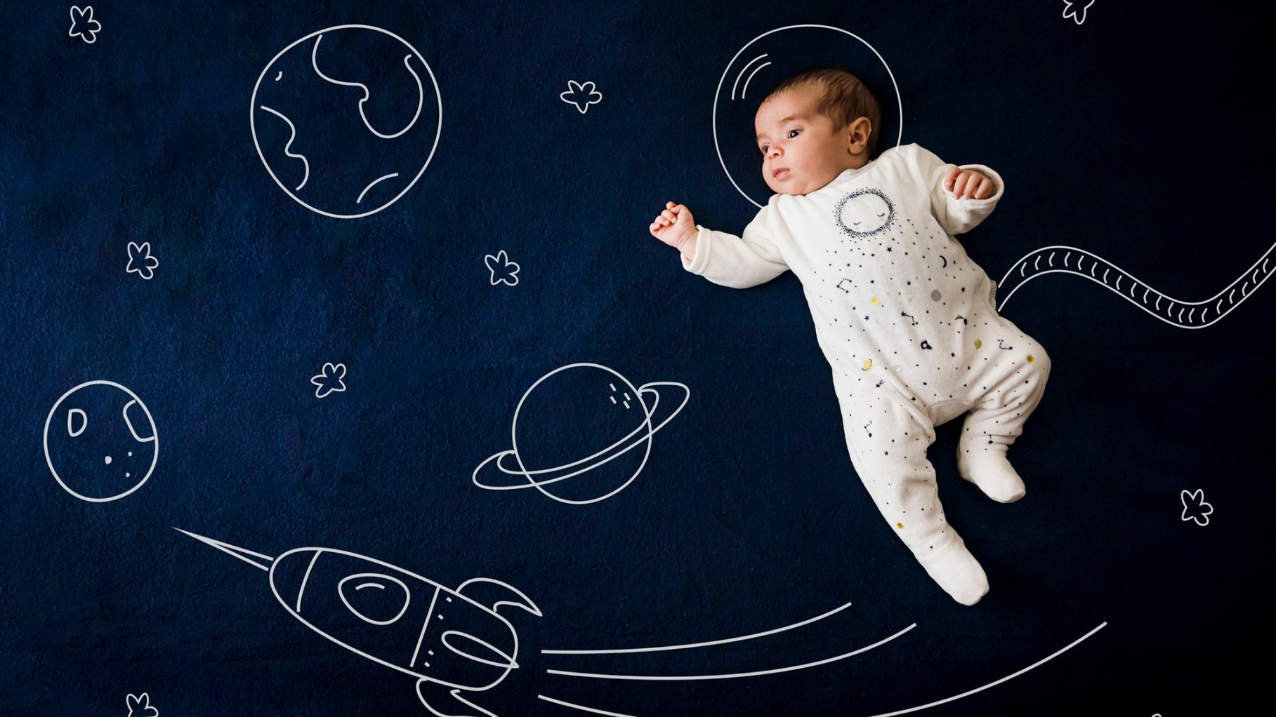 Baby boy on dark blue outer space background. He's head is in a space helmet.
