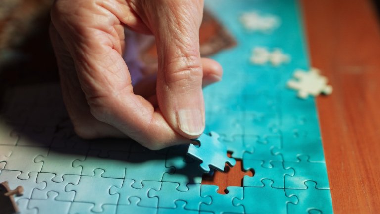 closeup of elderly woman's hand while she assembles jigsaw puzzle on wooden table;