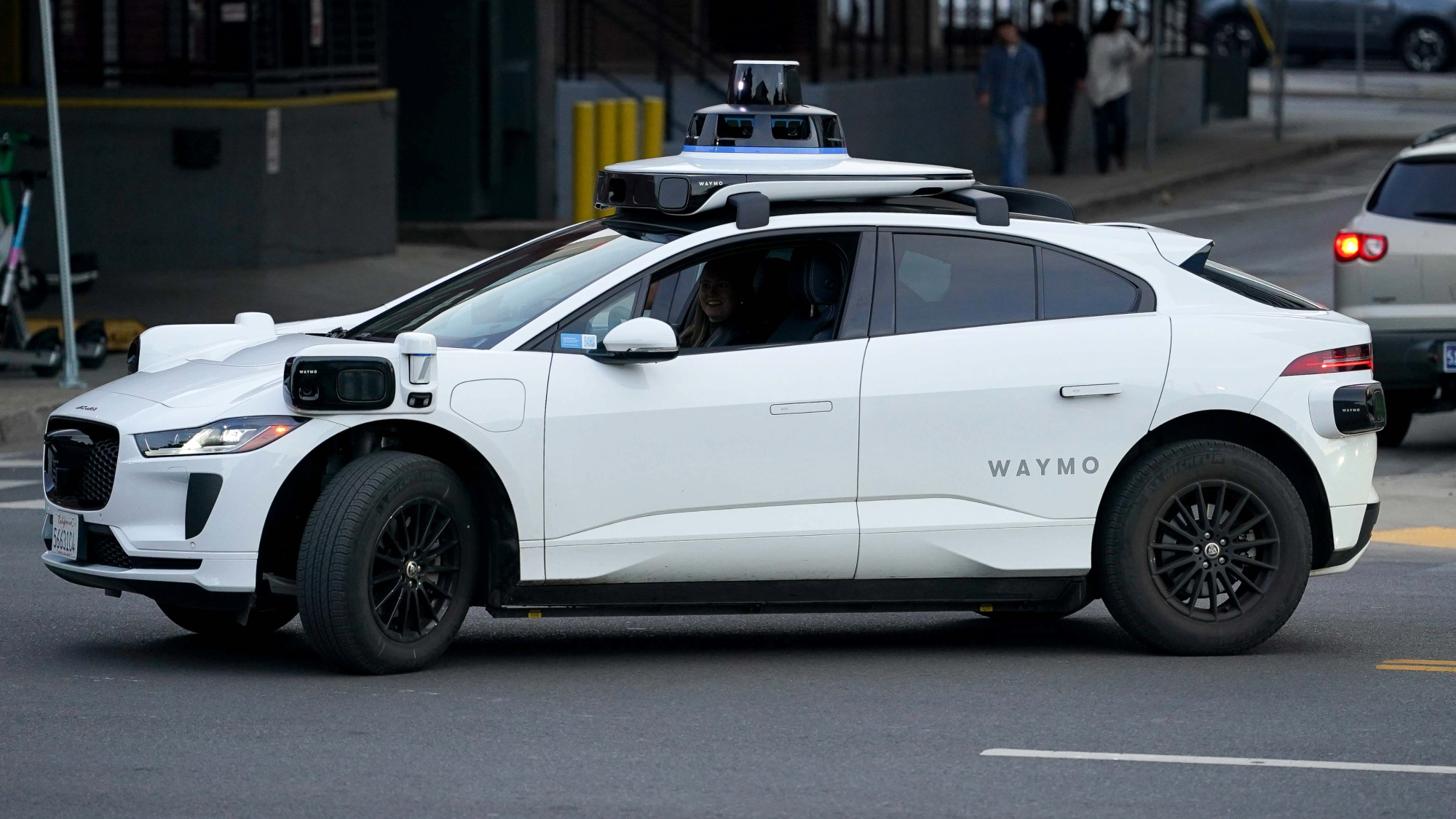 a white driverless car with a large black sensor on top on a city street