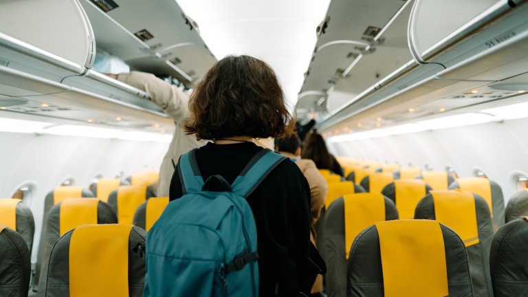 A caucasian young woman with a blue backpack looking for her seat in the airplain. Waiting in the row