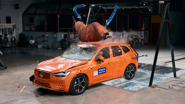 an orange car with a crash test dummy shaped like a moose in an indoor test facility