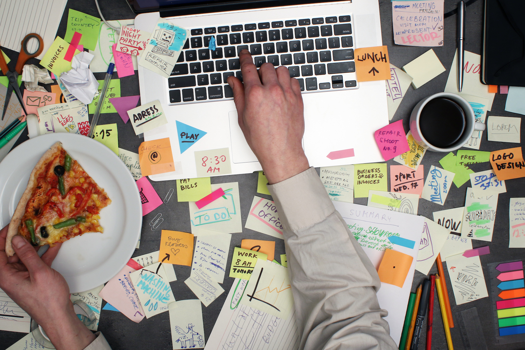 messy desk as someone works on their desk and eats pizza