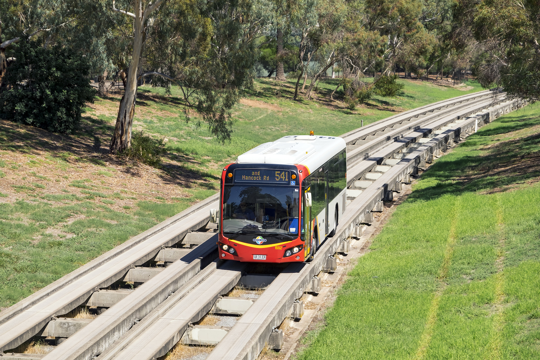 Adelaide, Australia - March 21, 2016: New series of Adelaide Metro bus on Route 541 heads away from the city centre along the O-Bahn guided Busway with a backdrop of trees and open space. Opened in 1986 after a light rail (tram) extension was rejected, the Daimler-Benz O-Bahn system runs on specially-built concrete track incorporating elements of both bus and rail systems. Adelaide’s unique busway is 12km (7.5mi) long and incorporates 3 interchange stations.