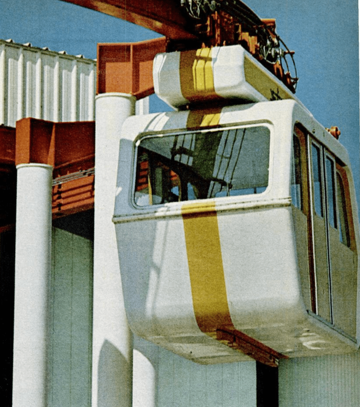 Vintage photograph showing a suspended car that hangs from a track on the roof. The car is white with a yellow stripe.