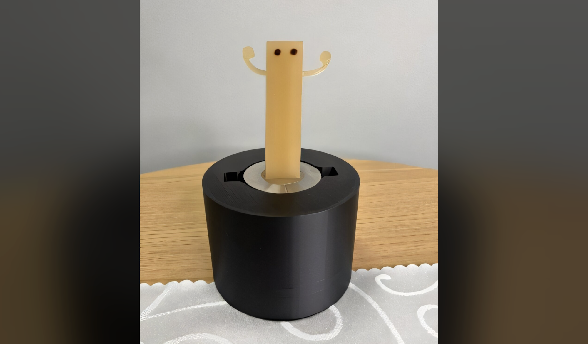 a robot standing on a black circular base. on top of it is a rectangle made of gummy candy with wavy arms and two dots for eyes