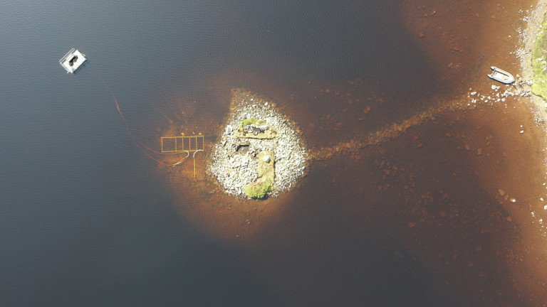 an aerial view of a lake in scotland with a human made island visible underneath the water