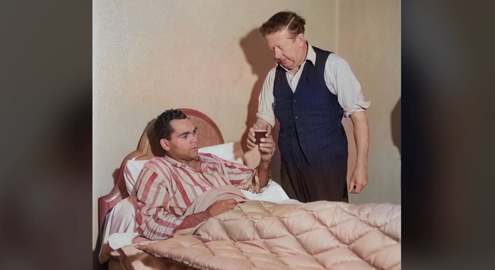 man in bed take a cup of liquid from another man