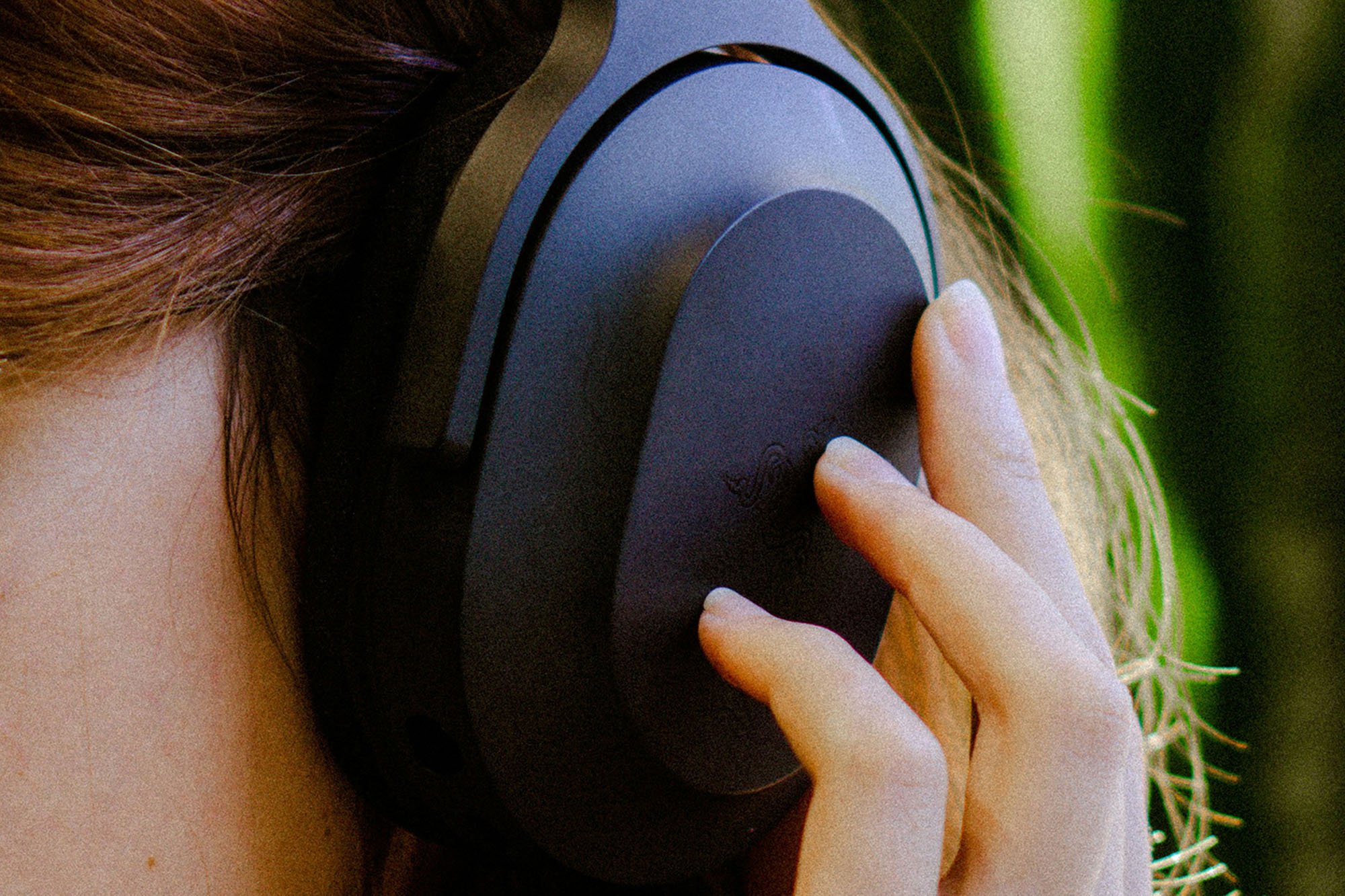Woman's fingers touching the capacitive sensor surface of some wireless headphones on her head