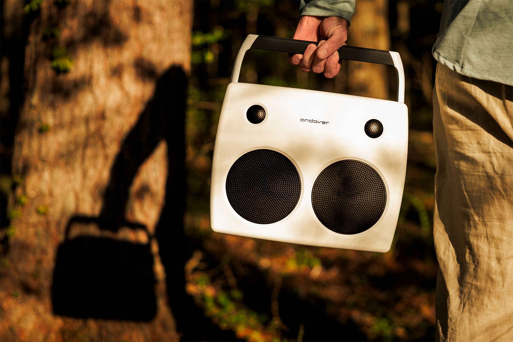 An Ivory Andover FreePlay speaker casting a shadow against a tree trunk
