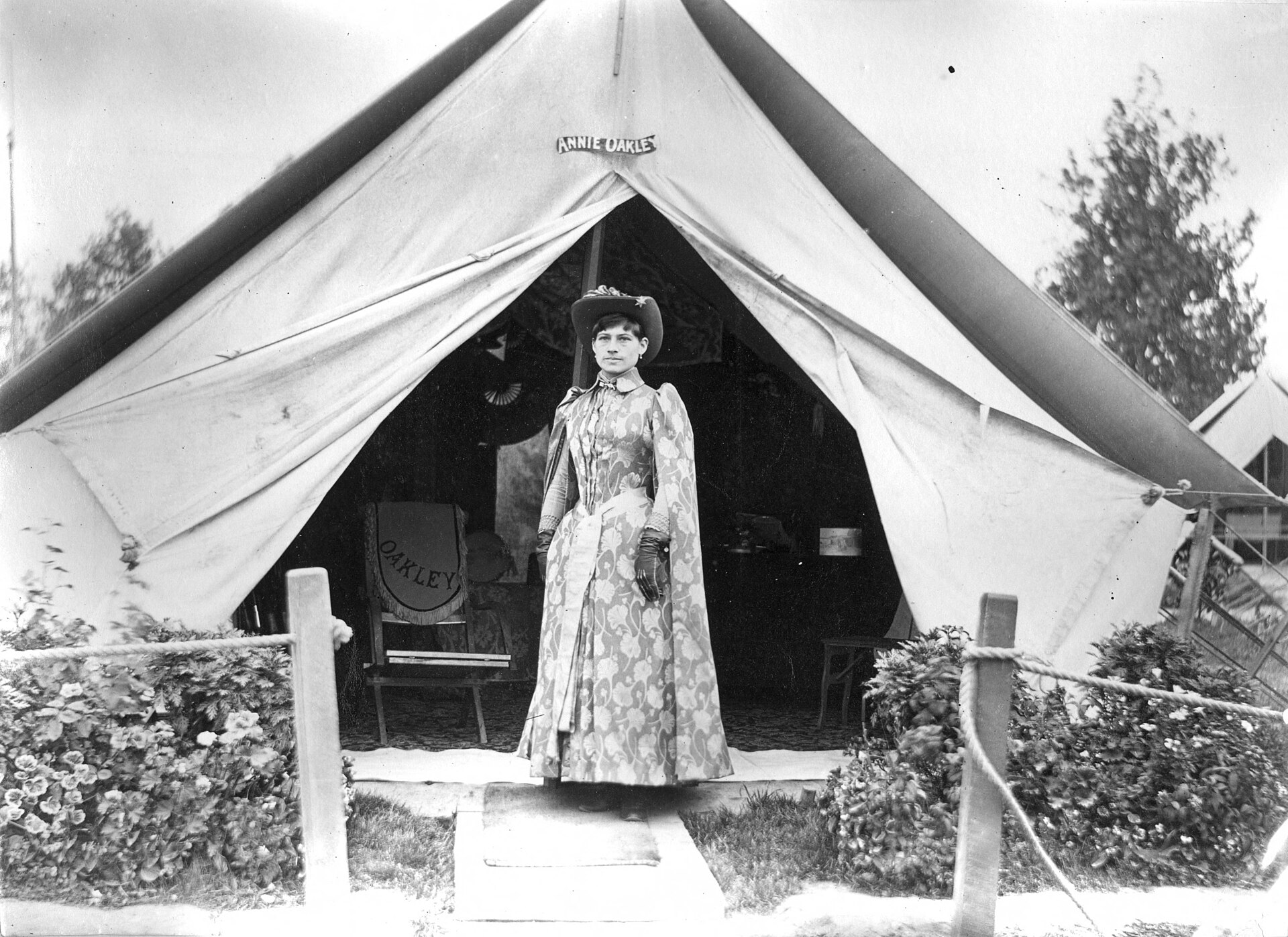 Young woman in dress with cape poses in front of a tent.