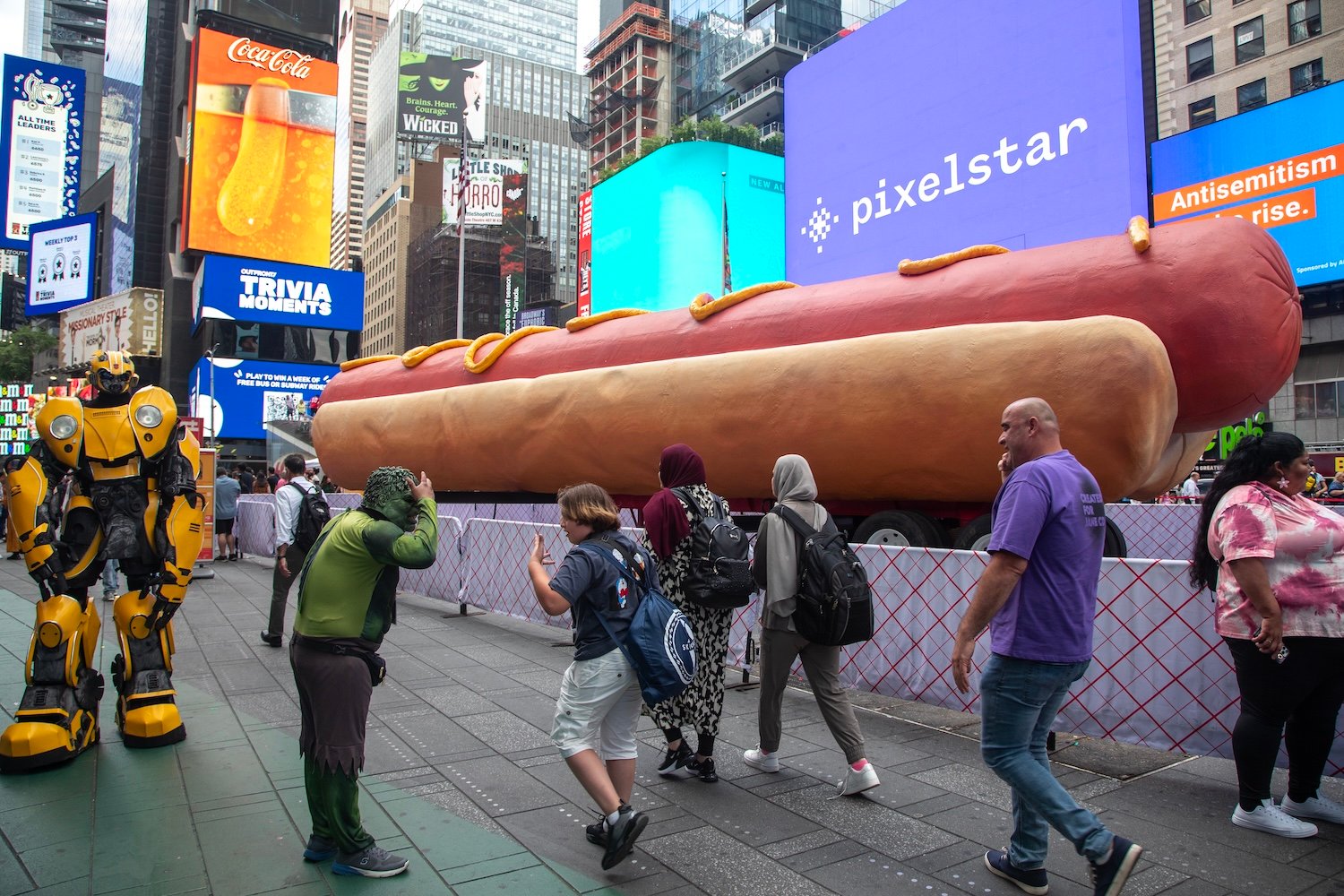 NEW YORK, NY - JUNE 12: People walk by a Hot Dog sculpture at Times Square on June 12, 2024 in New York City. At 65 feet long, Times Squares latest major public art installation, Hot Dog in the City, tops the record for the World's Largest Hot Dog Sculpture. (Photo by Liao Pan/China News Service/VCG via Getty Images)