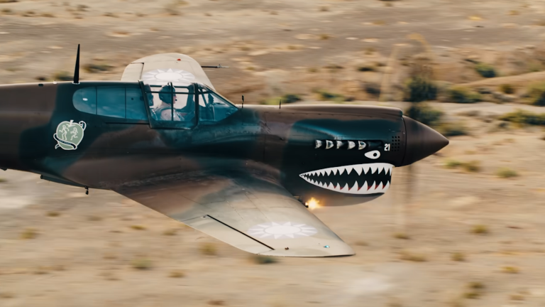 Side view of P-40 fighter plane firing its machine guns midflight in the desert