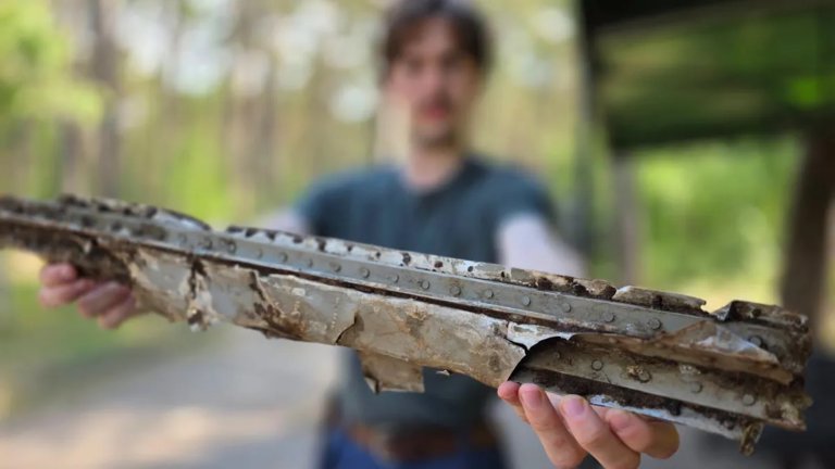 Close up of WW2 airplane wreckage piece held by man who is out of focus in the background