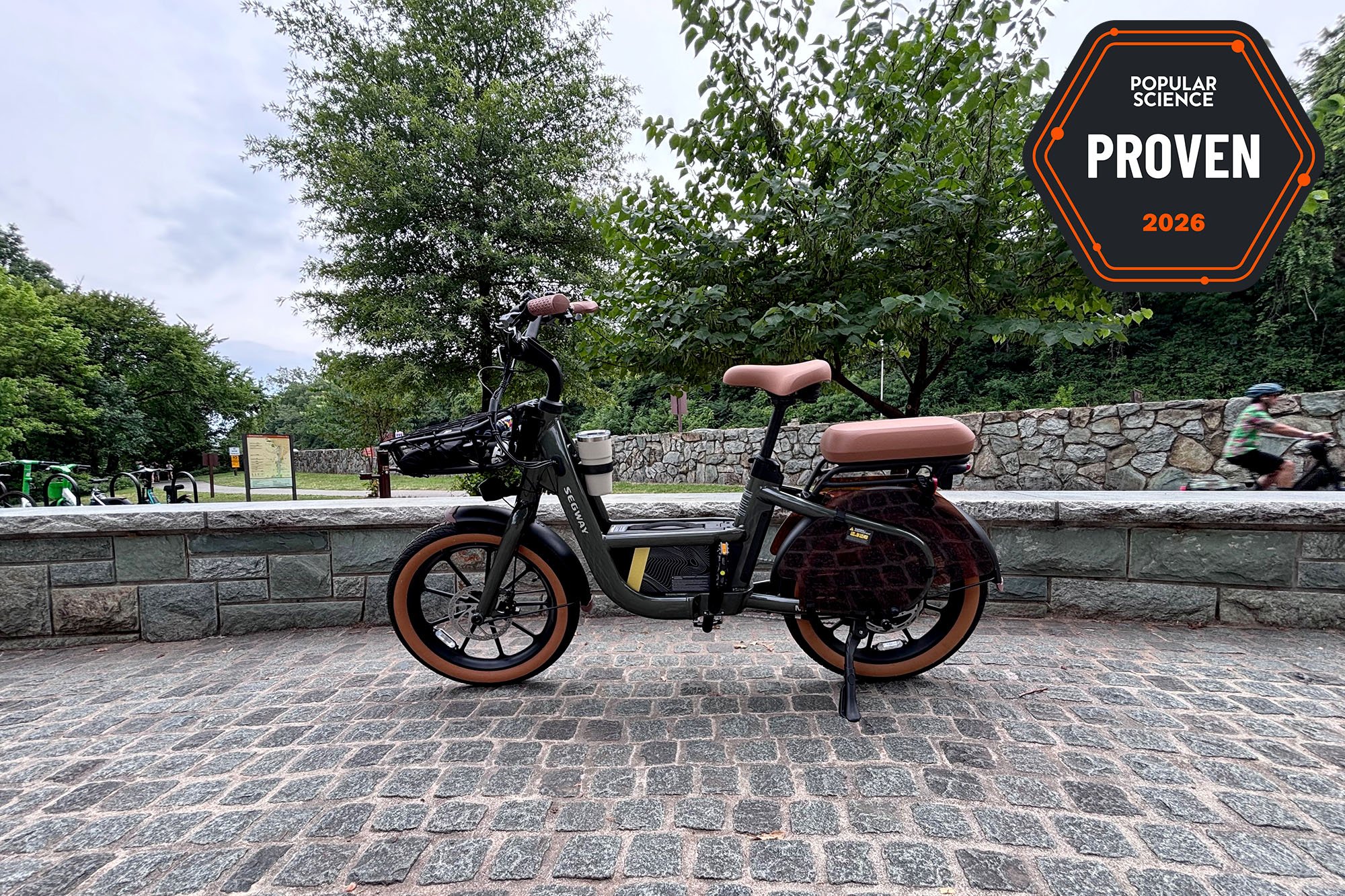 The Segway MUXI cargo e-bike sitting on cobblestones beside the Mount Vernon bike path at the entrance to Theodore Roosevelt Island. The PopSci Priven badge is shown in the top right corner.