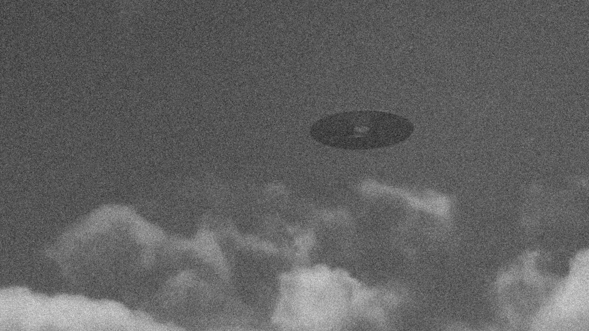 Bad quality photo of U.F.O. in sky. Black and white grainy photo of circular alien flying object. Sky with clouds and unknown spaceship.