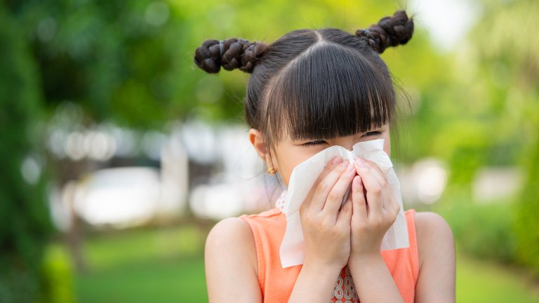 Small Asian girl blowing her nose into a napkin.