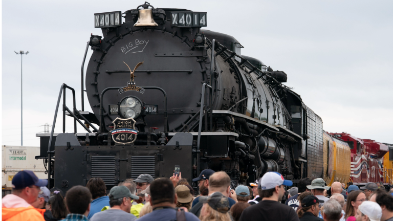 a large steam train with a crowd of people surrounding it