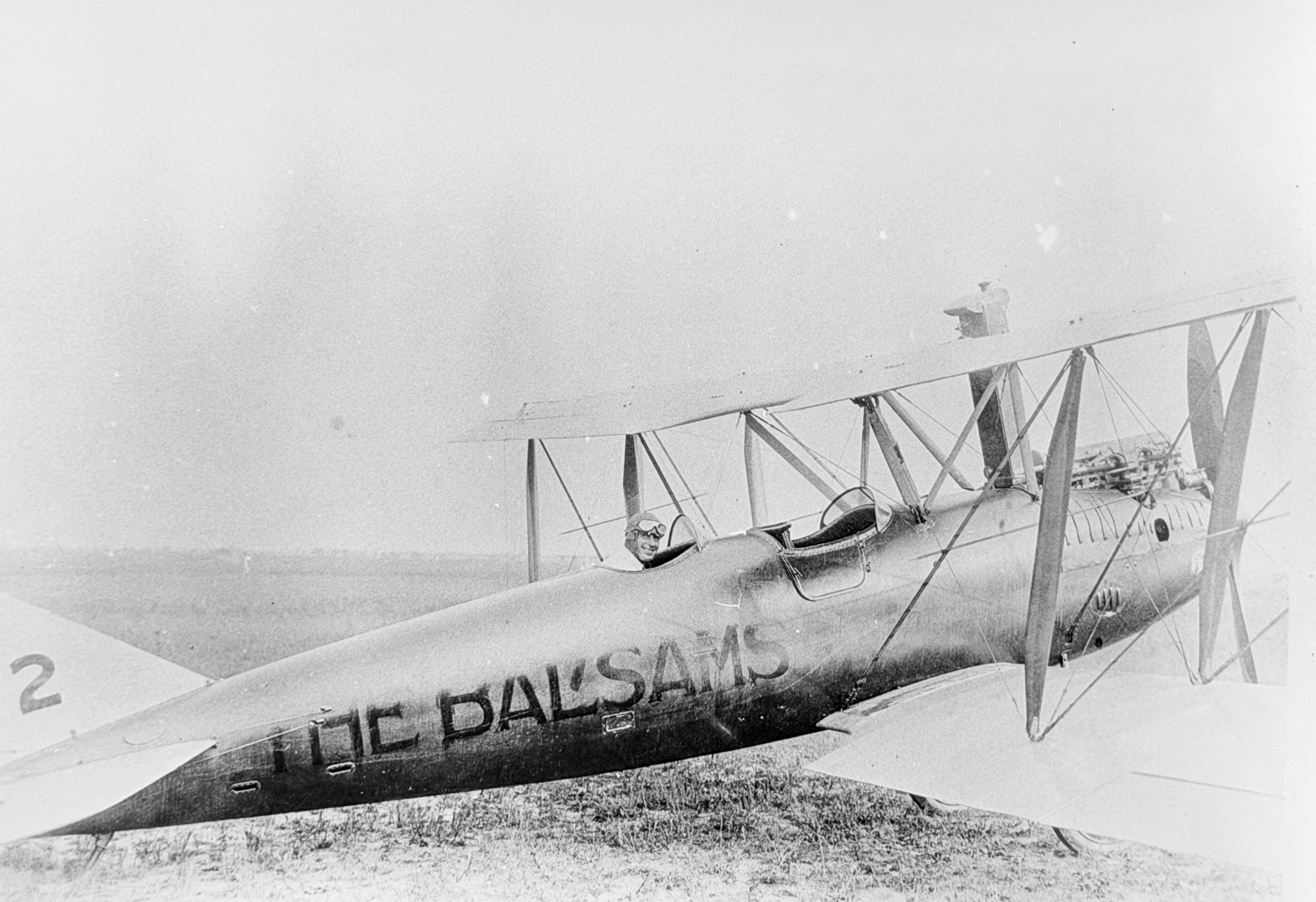 a black and white photo of a pilot sitting in the back seat of a biplane in 1920. the plane has 