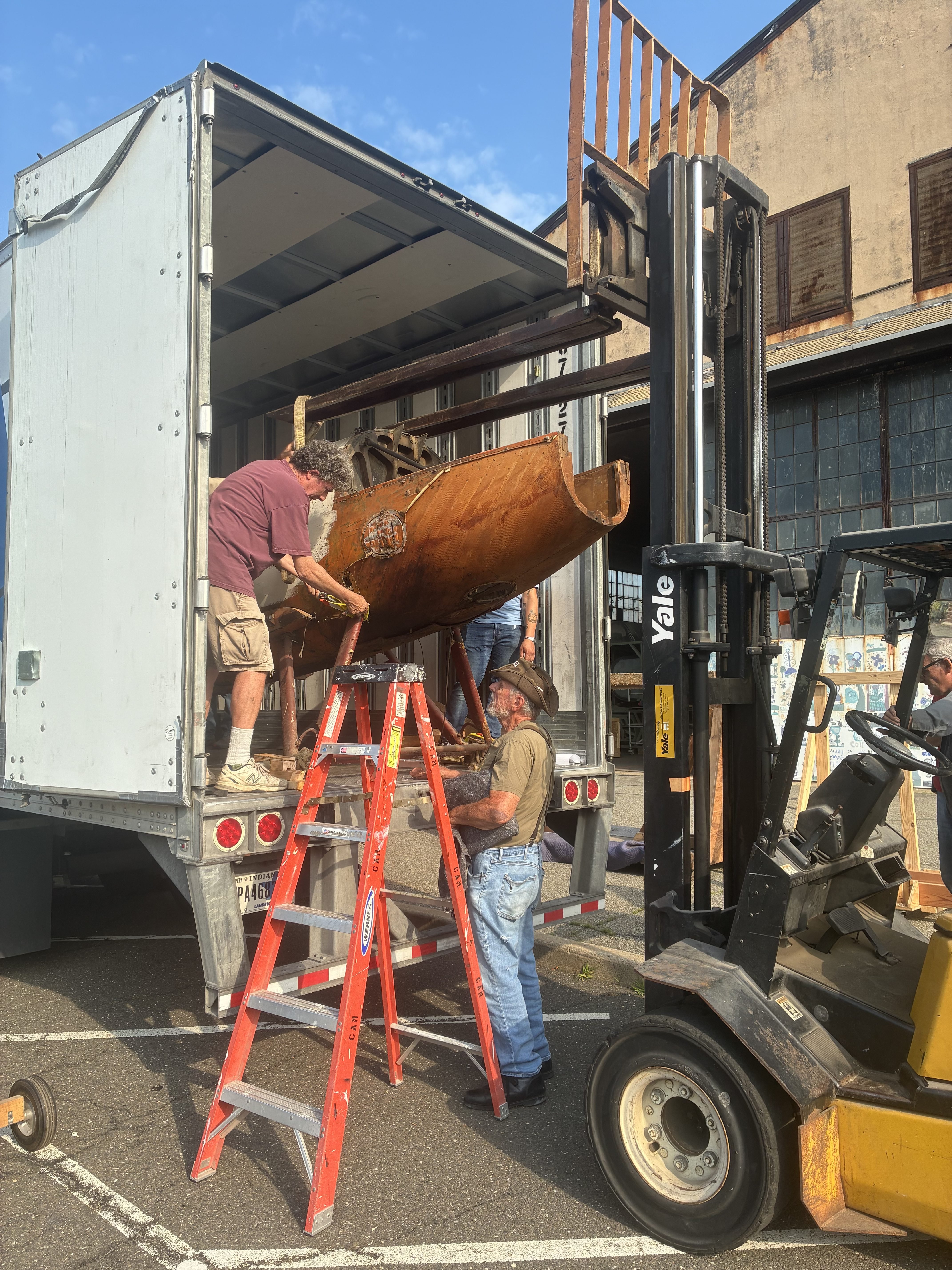 four men unload a wooden plane body from a white truck