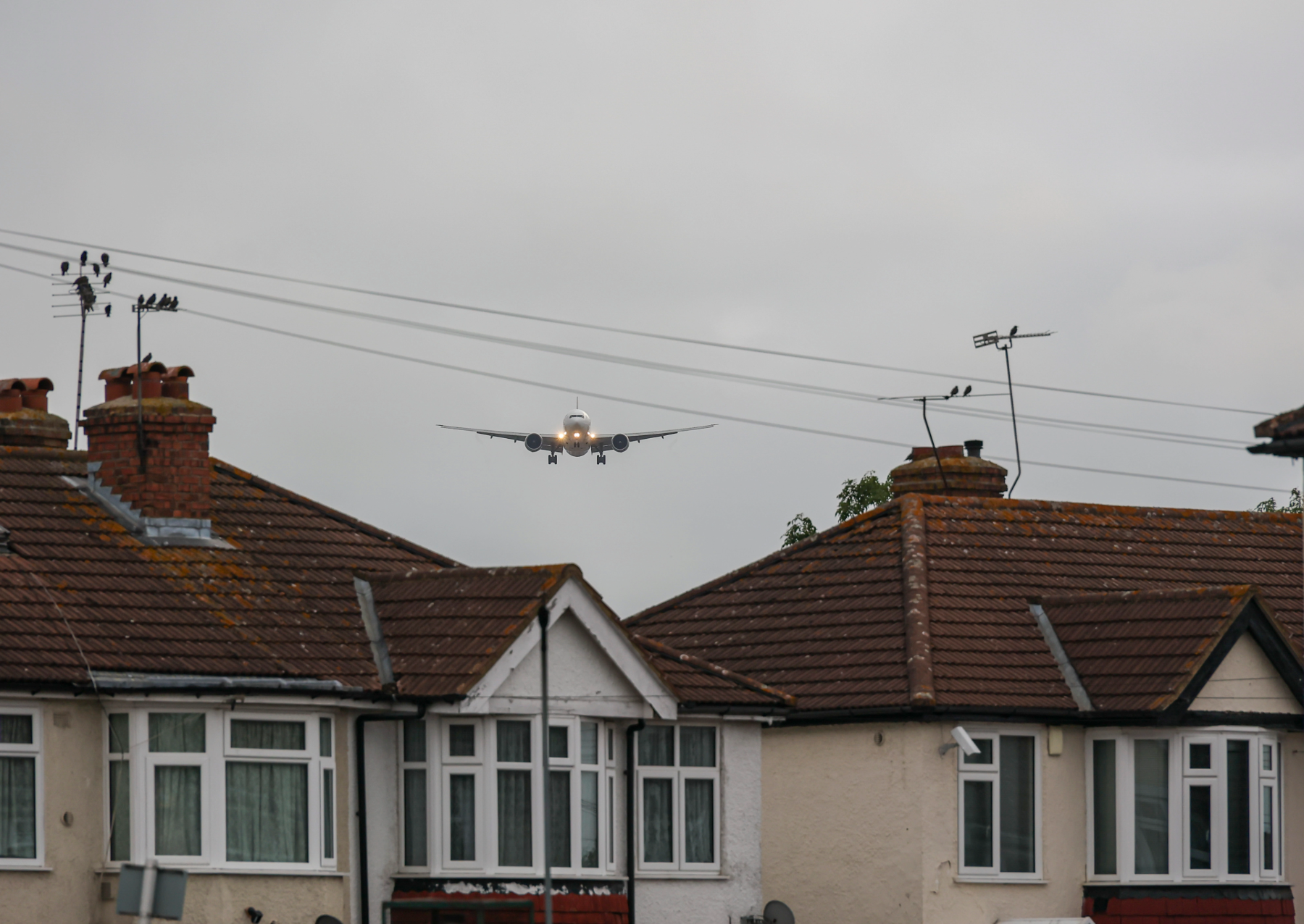 a singapore airlines plane beginning its descent between two houses with red roofs