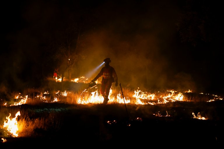 Firefighter with headlamp in the dark surrounded by low blazes.