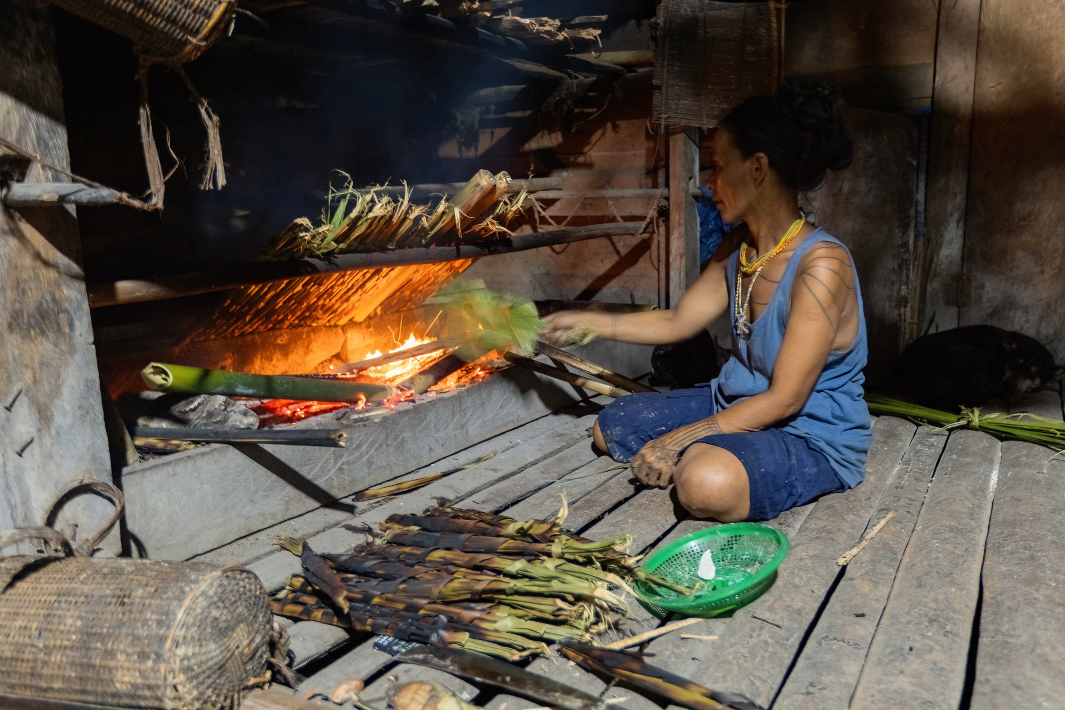 Mentawai woman cooking in the kitchen in the traditional house in the village on Siberut island West Sumatra Indonesia. She wears blue and has tattoos.