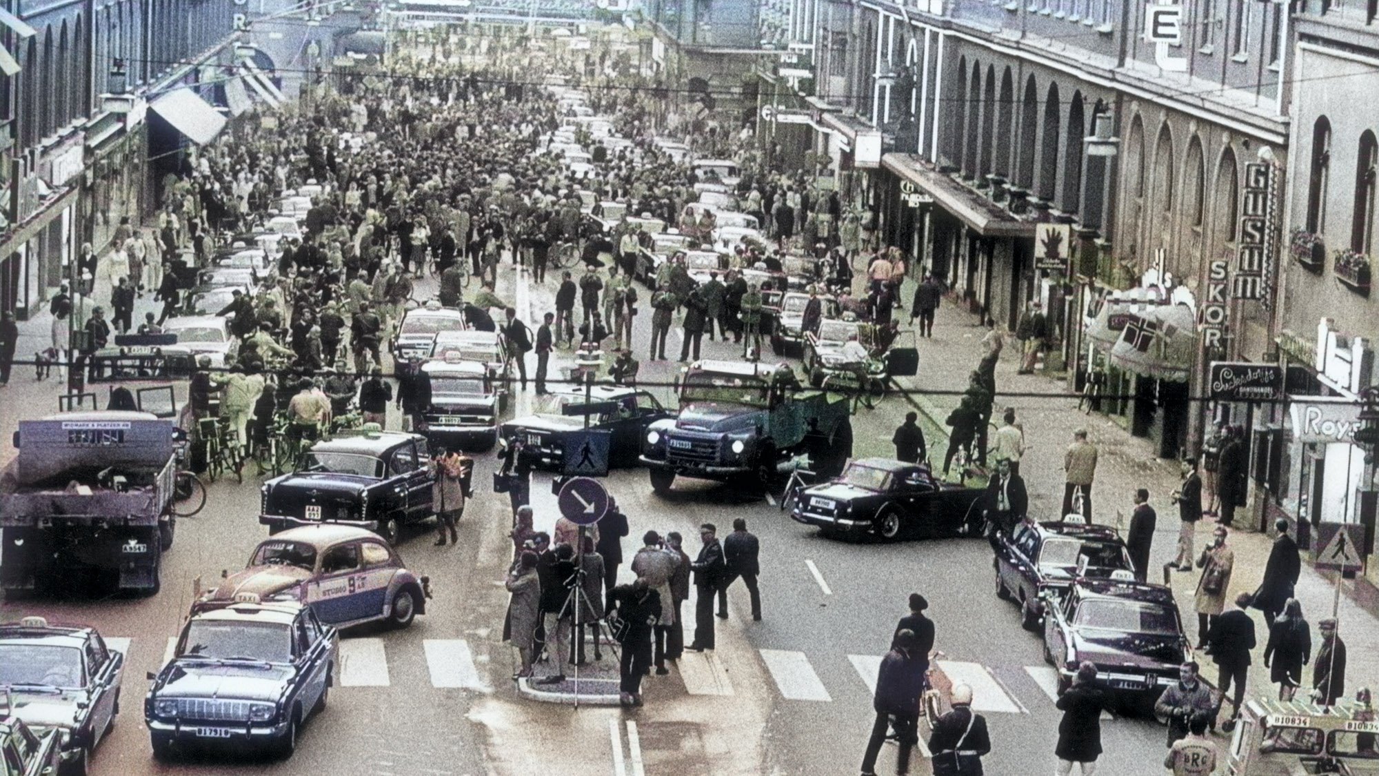 Vintage colorized photographof road in Sweden with cars jammed and many people walking.