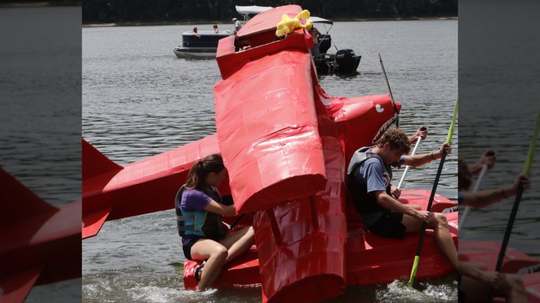Two people piloting a cardboard boat designed to look like a red biplane during the Cardboard Boat Regatta in New Richmond, Ohio