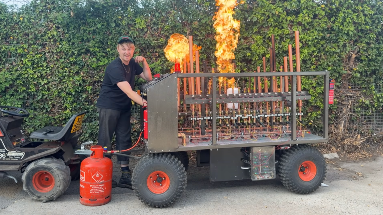 Man standing next to his flame-spouting pipe organ invention powered by propane.