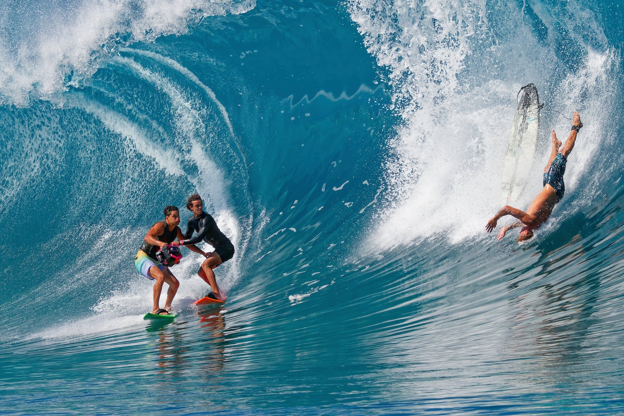 Three surfers converge on the same wave