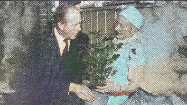 Colorized vintage photo of a woman in a blue dress and hat holding a peanut plant with a man in a suit.