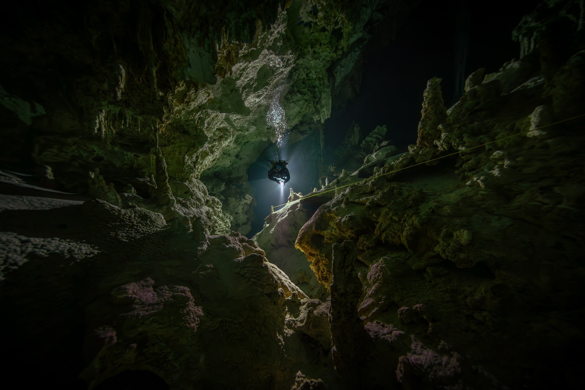 A cave diver follows a yellow guideline through winding passages 