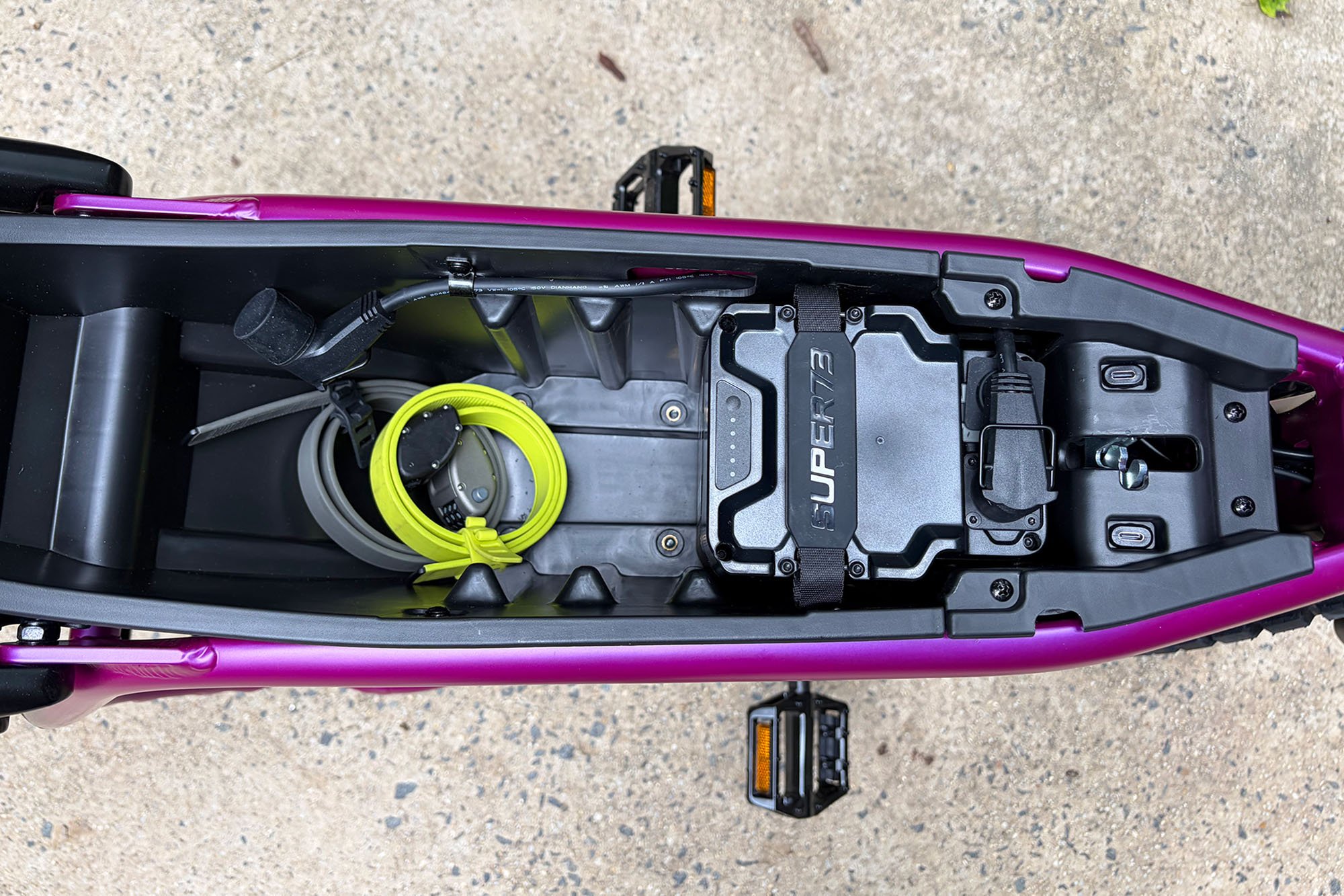 The open compartment of a Super73-MZFT e-bike from above showing the battery and a rolled up OTTOLOCK cinch lock