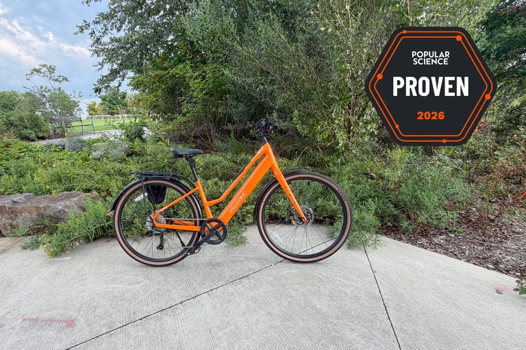 A sunset tangerine Velotric Tempo city commuter e-bike sitting in a green leafy nook