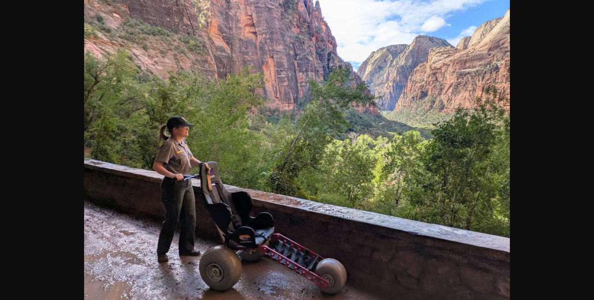 An all-terrain wheelchair with large balloon tires on a dirt trail in a canyon landscape.