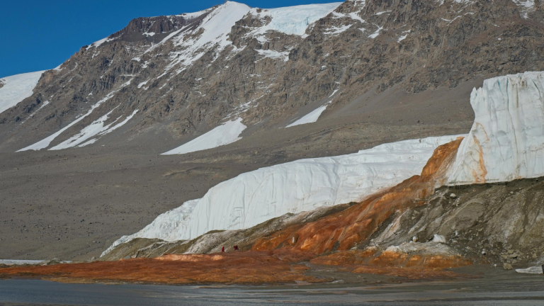 a reddish-orange waterfall near ice and gray rock