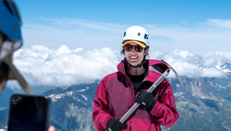 A woman holding a pick axe in front of the French Alps
