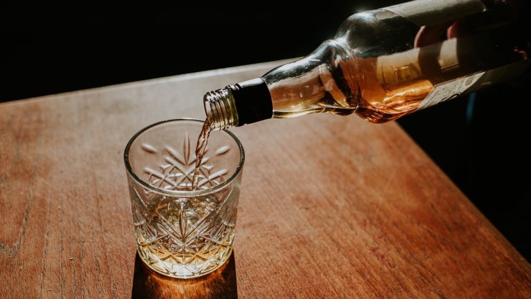 A bottle of whisky is poured into a cut glass tumbler over ice. Space for copy.