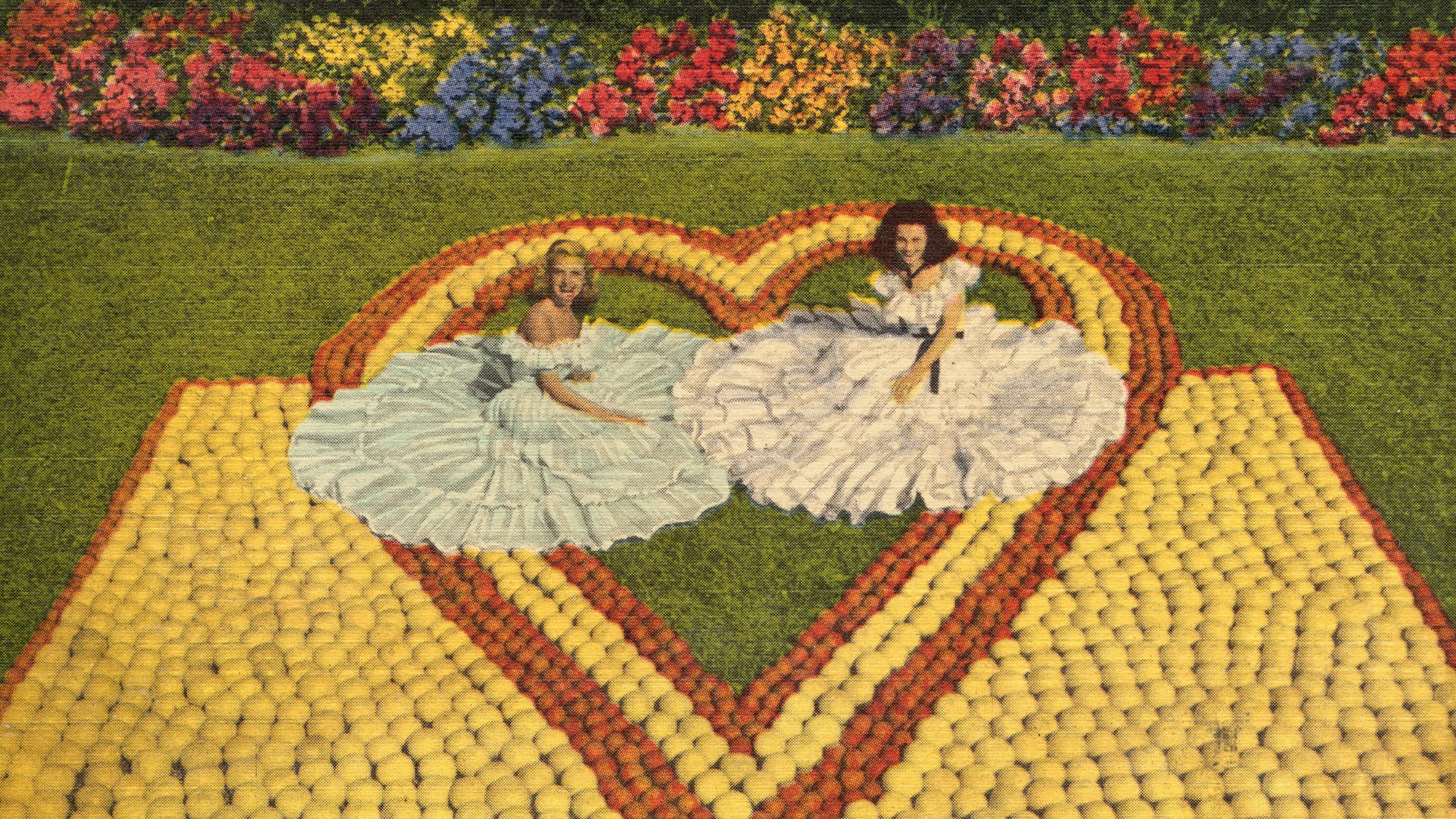 two women in big dresses pose wth the oranges and grapefruit in the shape of a heart.