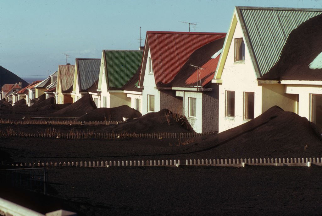 Homes with colorful roofs buried in black volcanic ash.